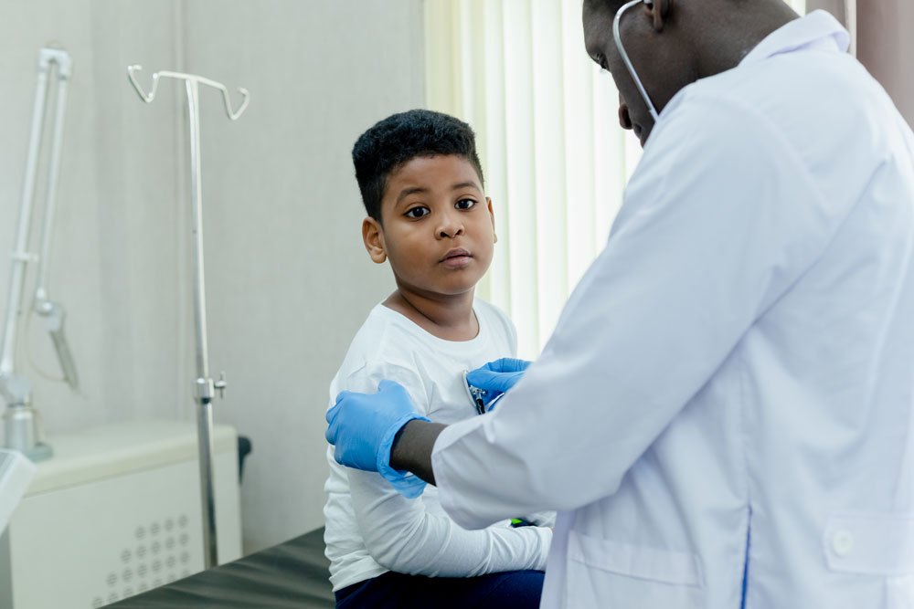 lack male doctor using a stethoscope to listen to a young child’s heartbeat during an exam at InterCommunity Health Care.