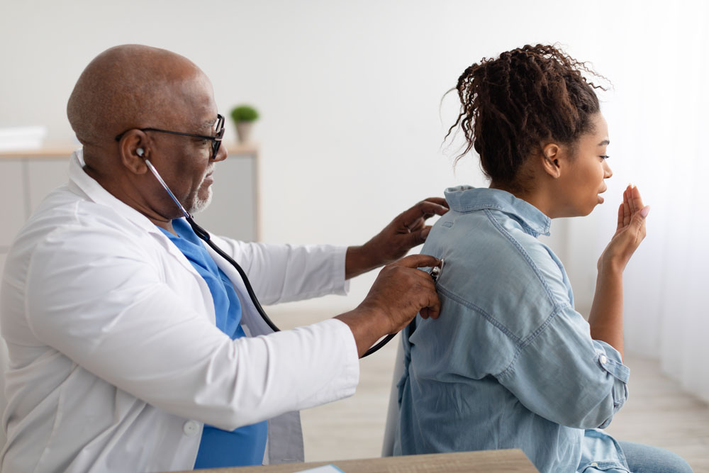 Black male doctor checking a female patient’s breathing during a medical exam at InterCommunity Health Care.